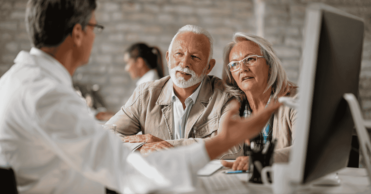 Senior couple talking with a financial advisor at a computer, discussing retirement investments and long-term savings plans.